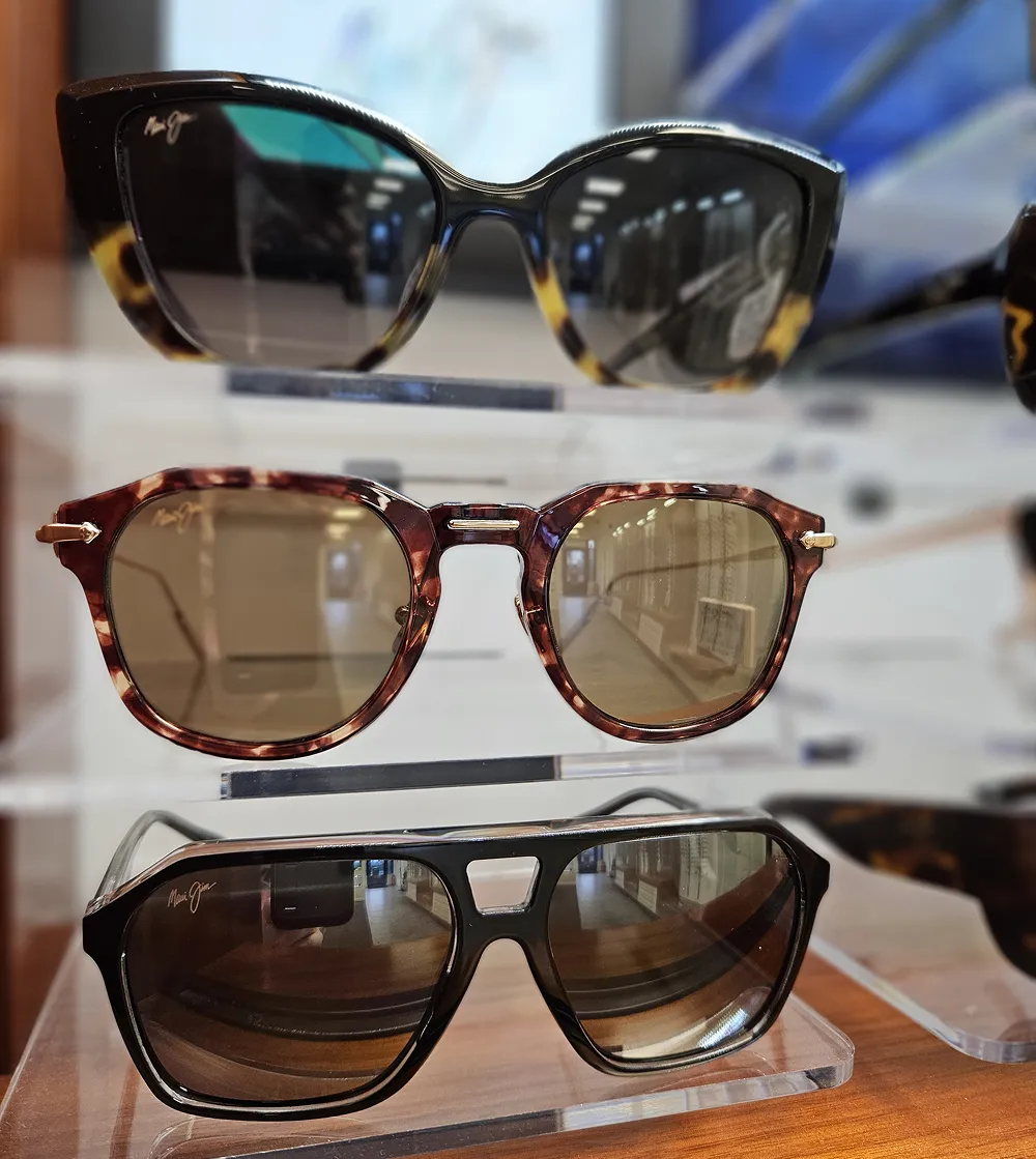 Three pairs of stylish Maui Jim sunglasses displayed on a clear stand in a store.