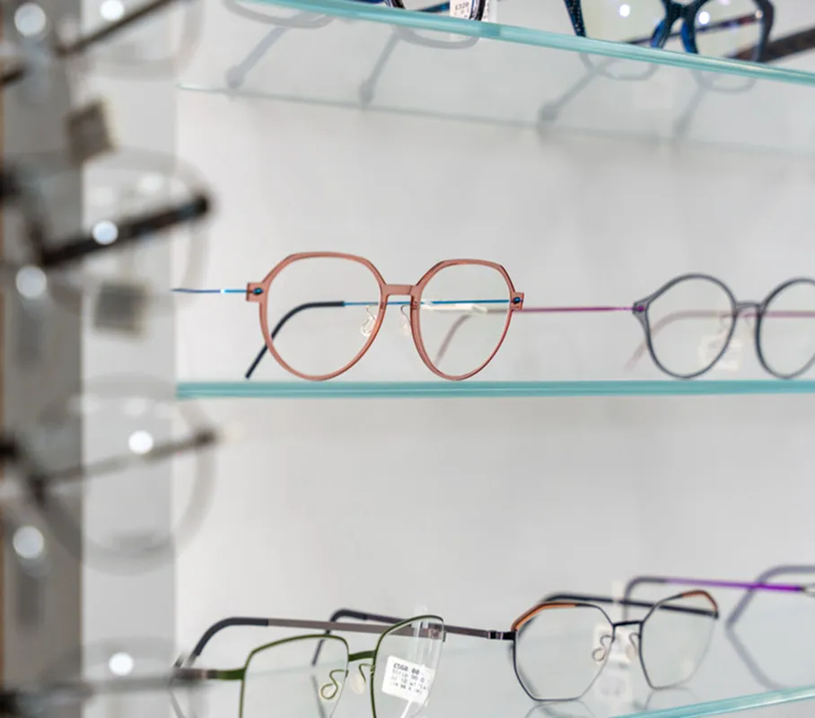 Various pairs of eyeglasses with thin metal frames displayed on glass shelves.