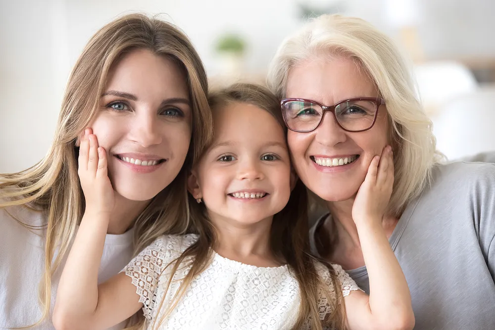 Three generations of women smiling together, with a young girl in the center touching the faces of two women beside her.