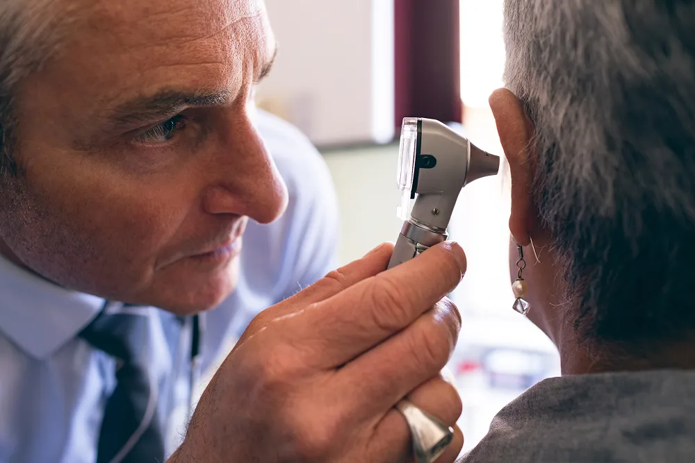 Doctor closely examining a patient's ear with an otoscope in a medical office.