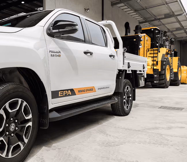 White Toyota Hilux pickup truck with EPA Mining Spares branding parked indoors near yellow heavy mining machinery.