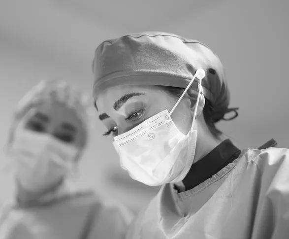 Two medical professionals wearing surgical caps, masks, and gowns in a clinical setting.