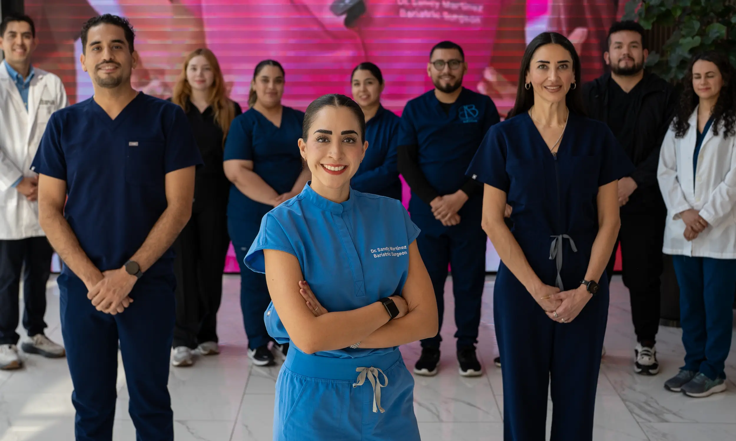 Smiling medical team in scrubs standing indoors with Dr. Sandy Martinez in blue scrubs at the front center.