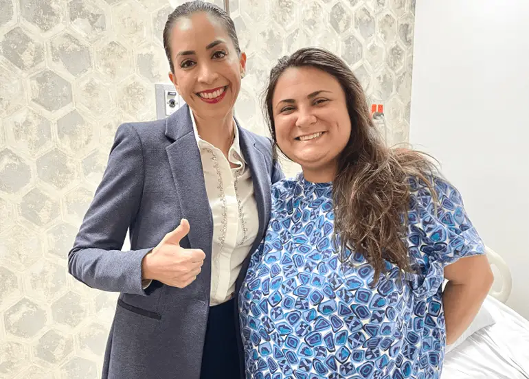 Dr. Sandy Martinez, bariatric surgeon, sharing a smile and a thumbs-up with a happy patient in her modern recovery room after a successful surgery.