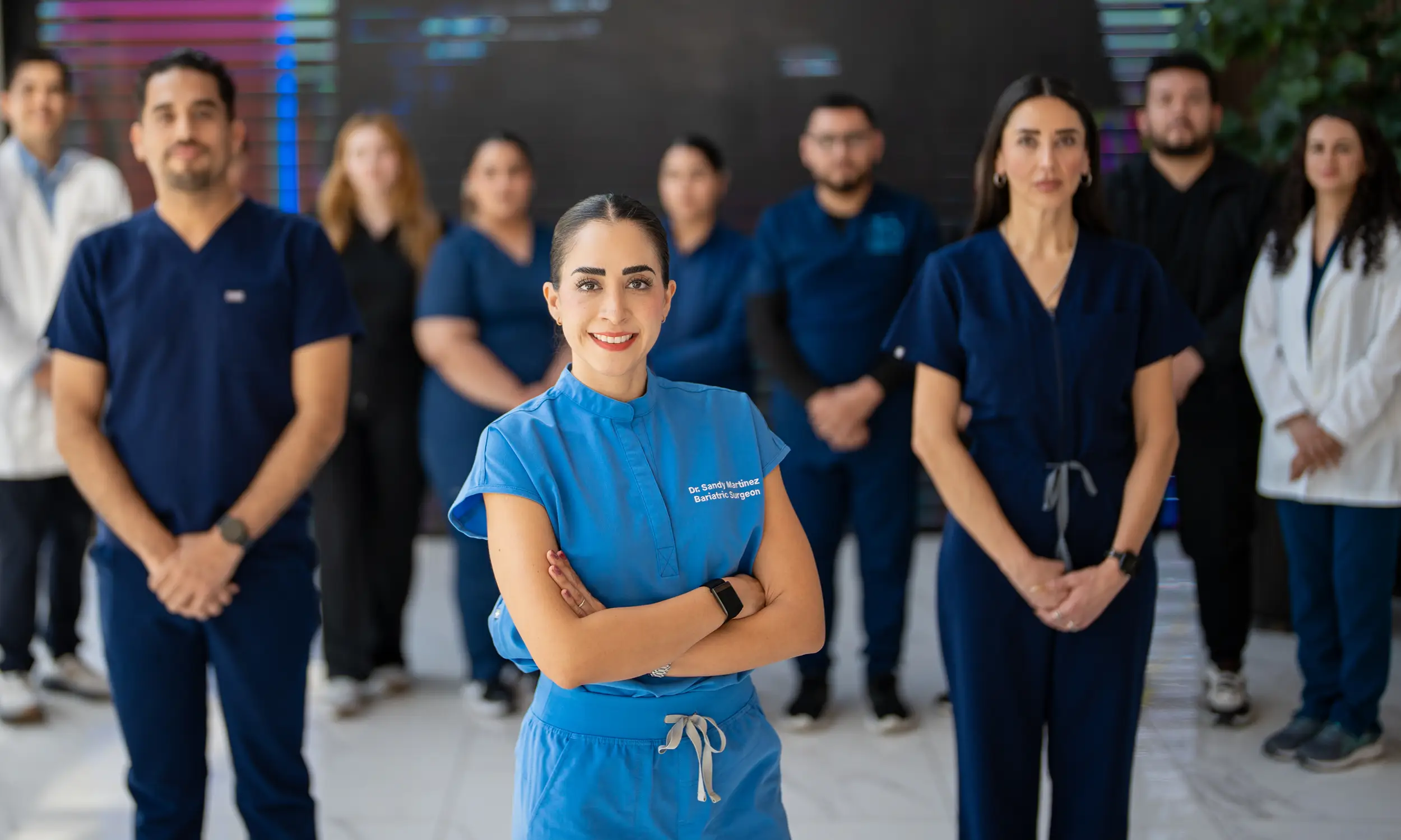 Medical team with a female bariatric surgeon in blue scrubs standing confidently at the front, surrounded by colleagues in uniforms and lab coats.