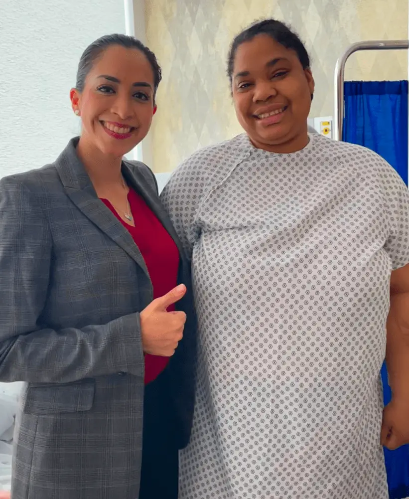 Smiling woman in a gray checkered blazer giving a thumbs-up next to a smiling woman in a hospital gown.