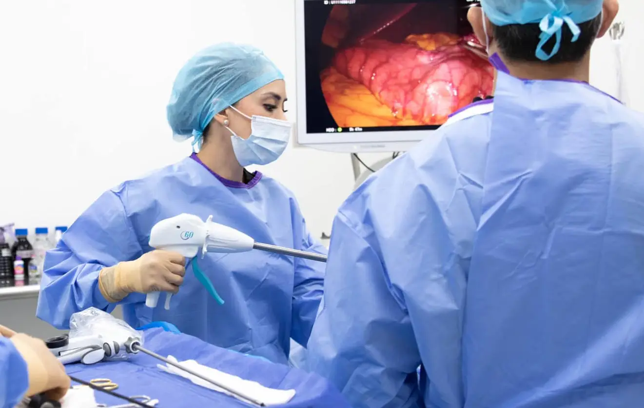 Surgeons in blue scrubs performing laparoscopic surgery while viewing internal organs on a monitor.