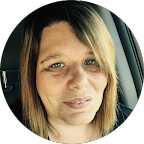 Close-up portrait of a woman with shoulder-length light brown hair, smiling slightly, sitting in a car.