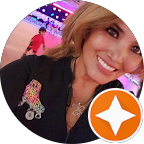 Smiling woman with blonde hair wearing a black shirt with colorful patches and an orange star badge overlay.