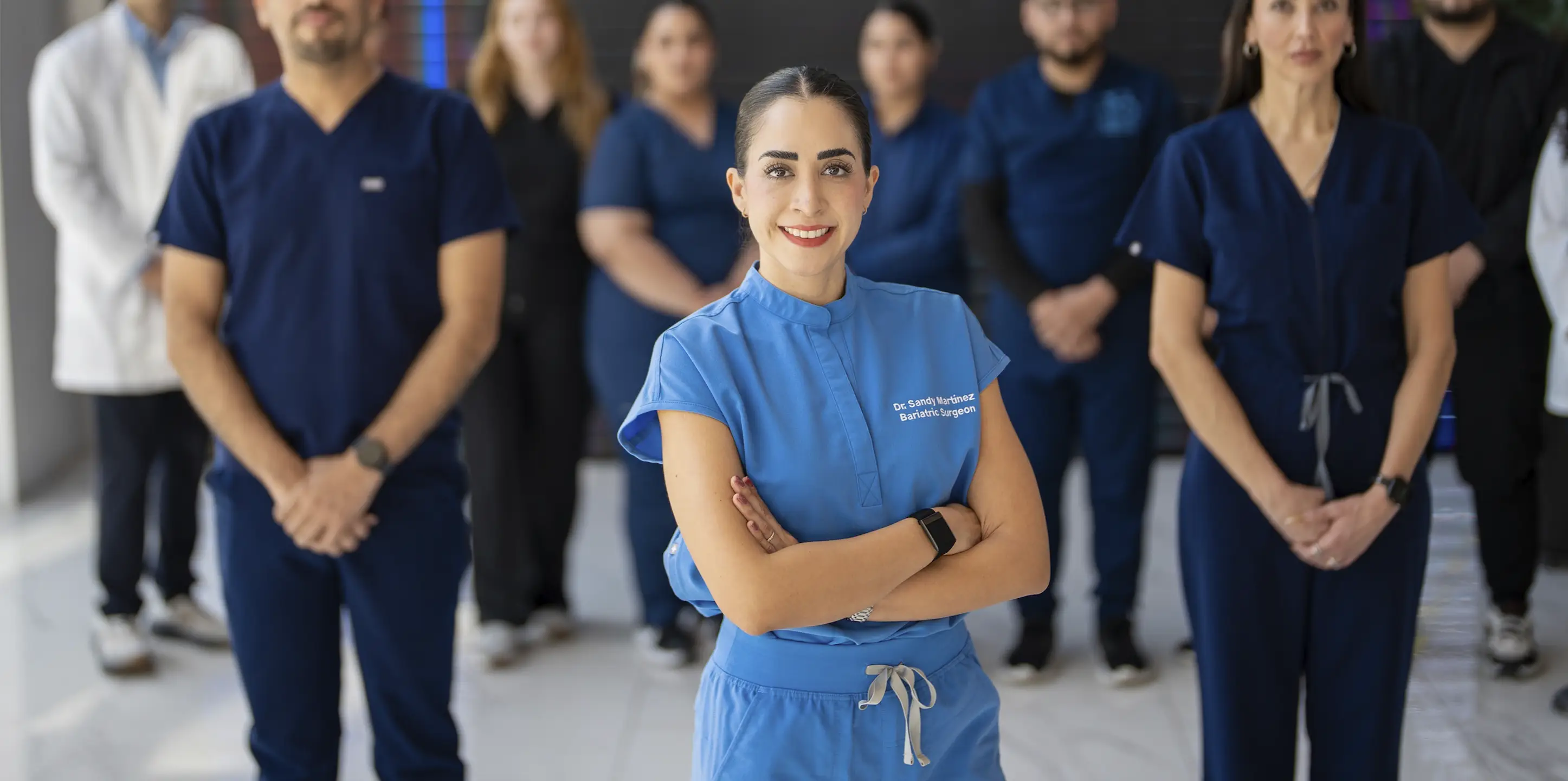 Dr. Sandy Martinez, leading bariatric surgeon in Tijuana, smiling with open arms in front of her expert multidisciplinary weight loss team.
