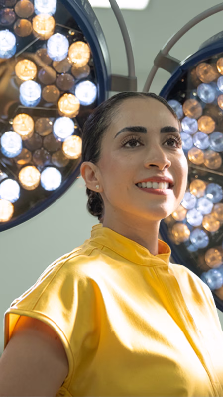 Dr Sandy Martinez in a bright yellow shirt smiling with surgical lights in the background.