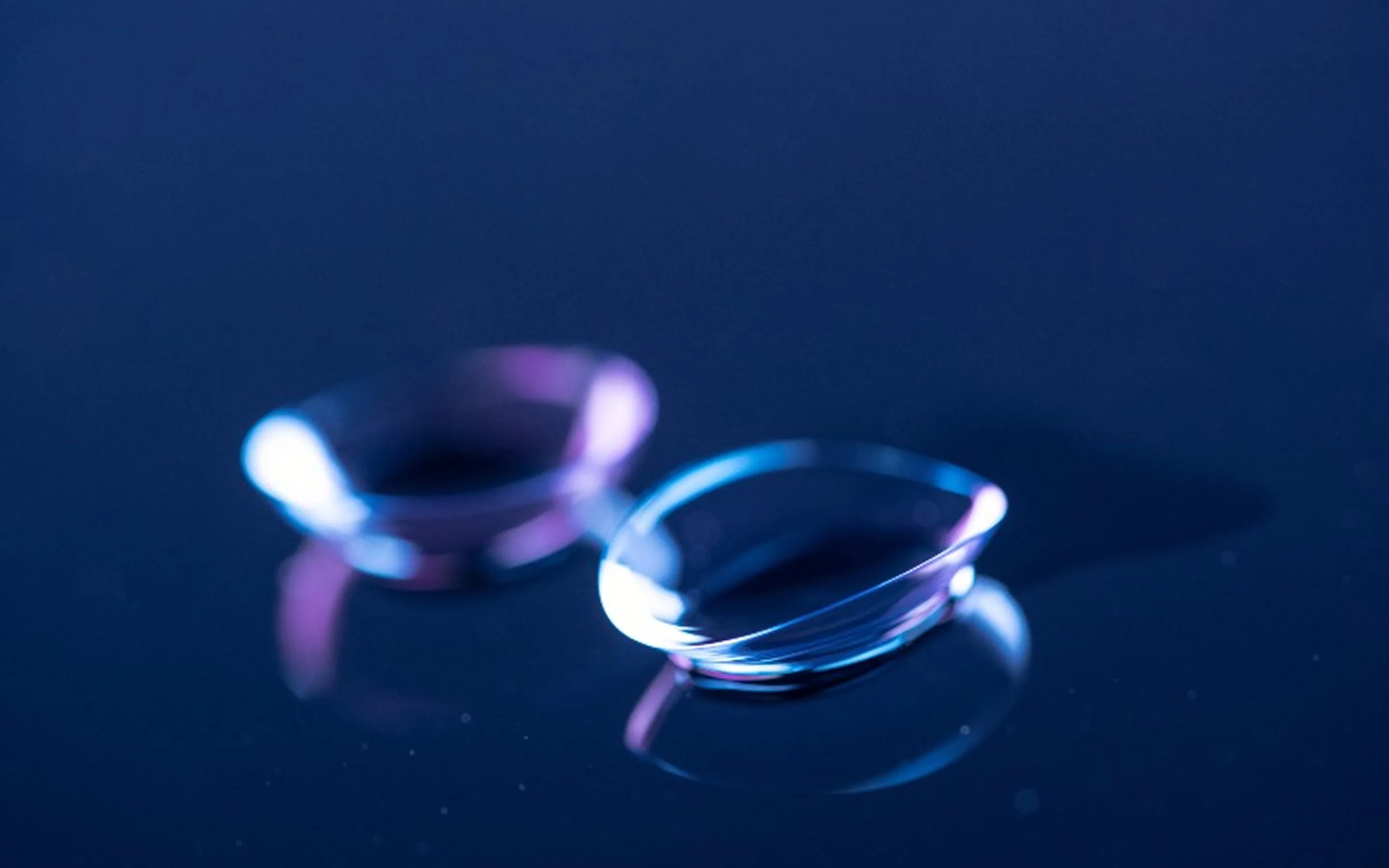 Two clear contact lenses with subtle blue and purple reflections on a dark surface.