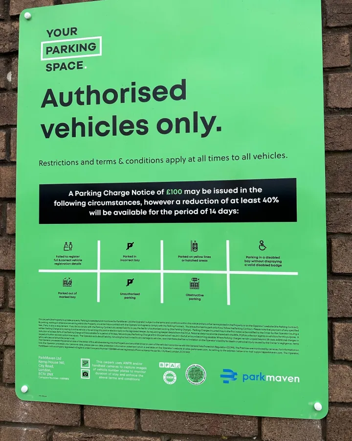 Green parking sign on a brick wall stating 'Authorised vehicles only' with parking charge notice details and icons indicating parking restrictions.
