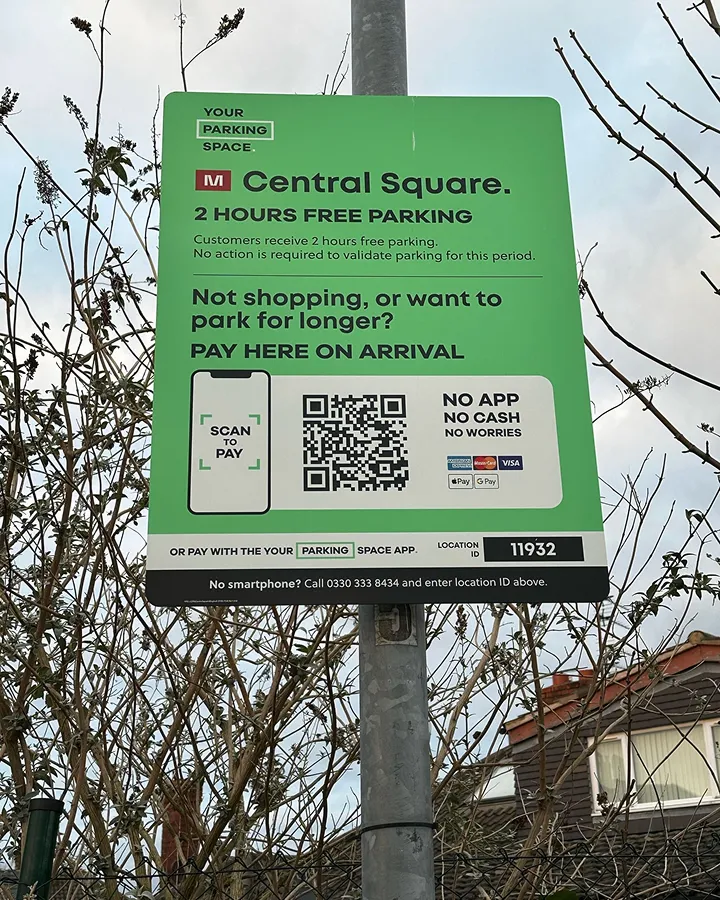 Green parking sign for Central Square offering 2 hours free parking with QR code for scan to pay option and location ID 11932.