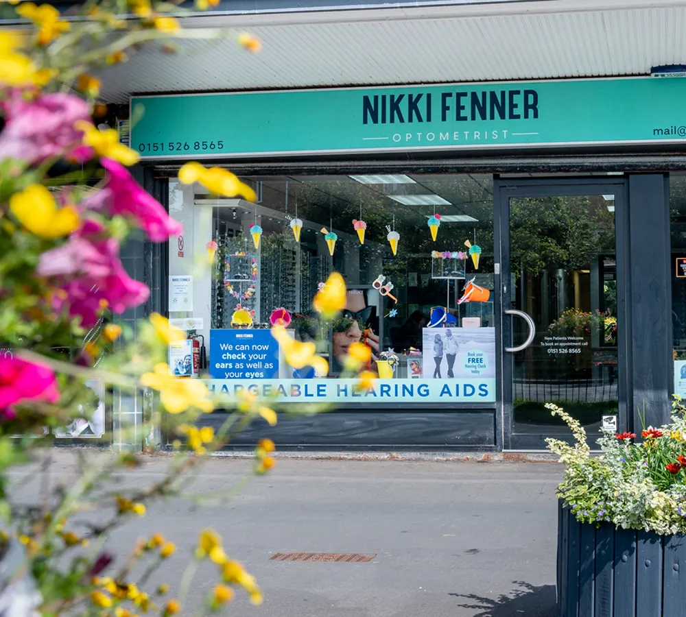 Storefront of Nikki Fenner Optometrist with colorful flower decorations in front and signs advertising hearing aid checks and free hearing checks.