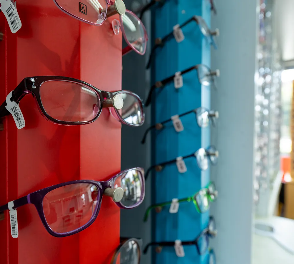 Display of various prescription eyeglasses with price tags on red and blue stands in an optical store.