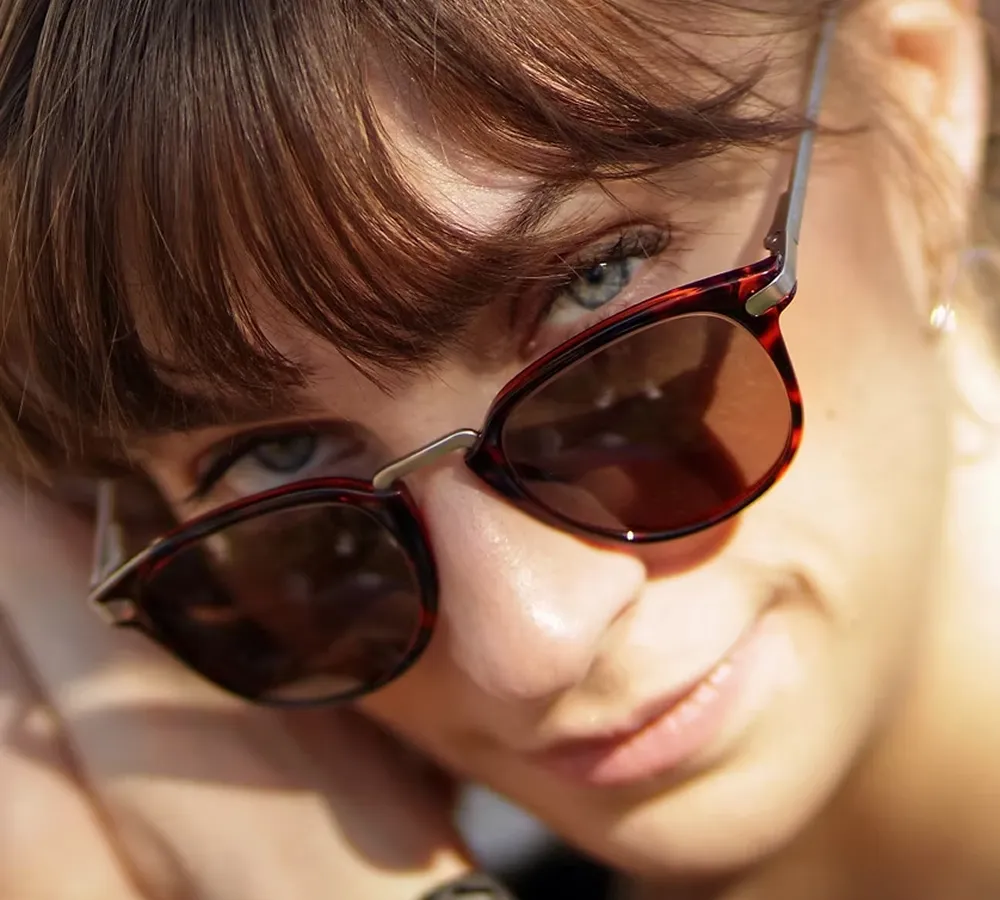 Close-up of a woman with light brown hair wearing tortoiseshell sunglasses lowered to reveal her blue eyes.