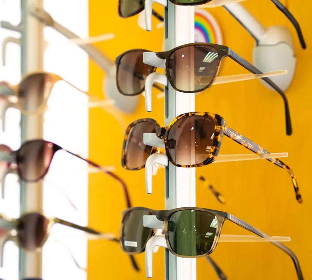 Multiple pairs of sunglasses with dark lenses displayed on a white rack against a bright yellow background.