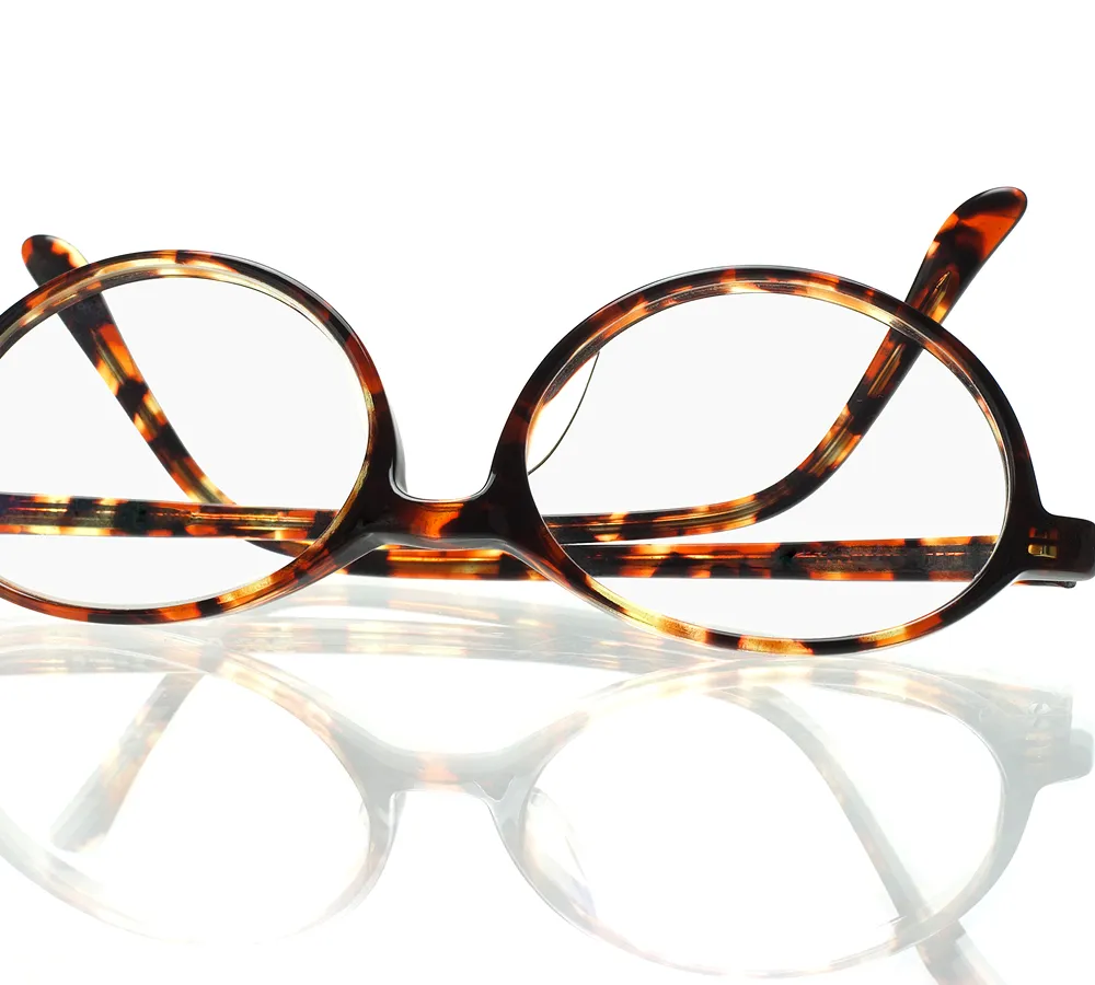 Round tortoiseshell designer eyeglasses with clear lenses on a white reflective surface.