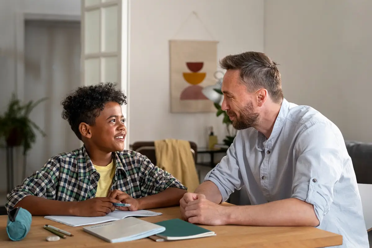 A father and son are seated at a table, engaged in learning with a notebook, representing home education.