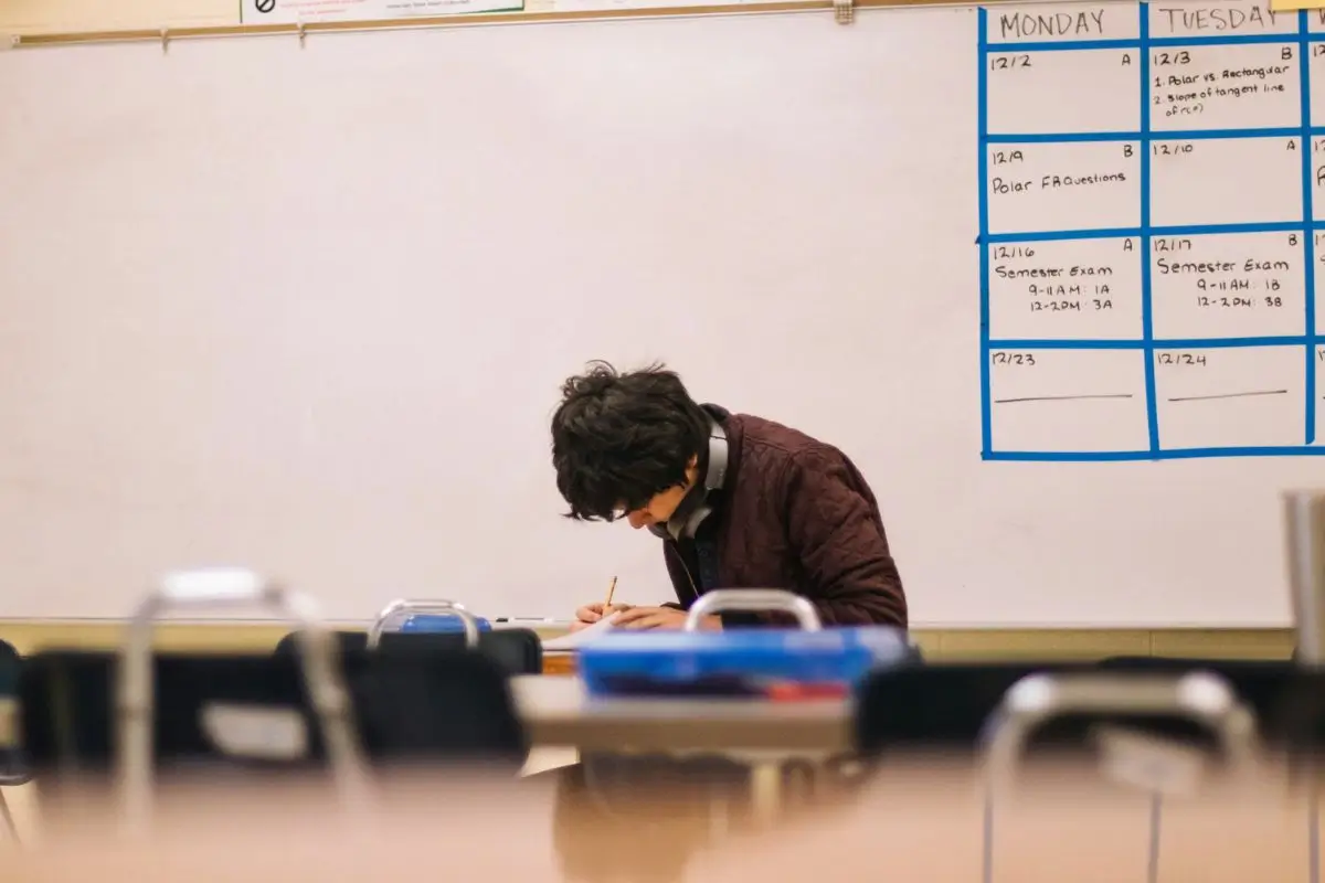 A student is sitting alone in an empty classroom, concentrating on understanding economics.