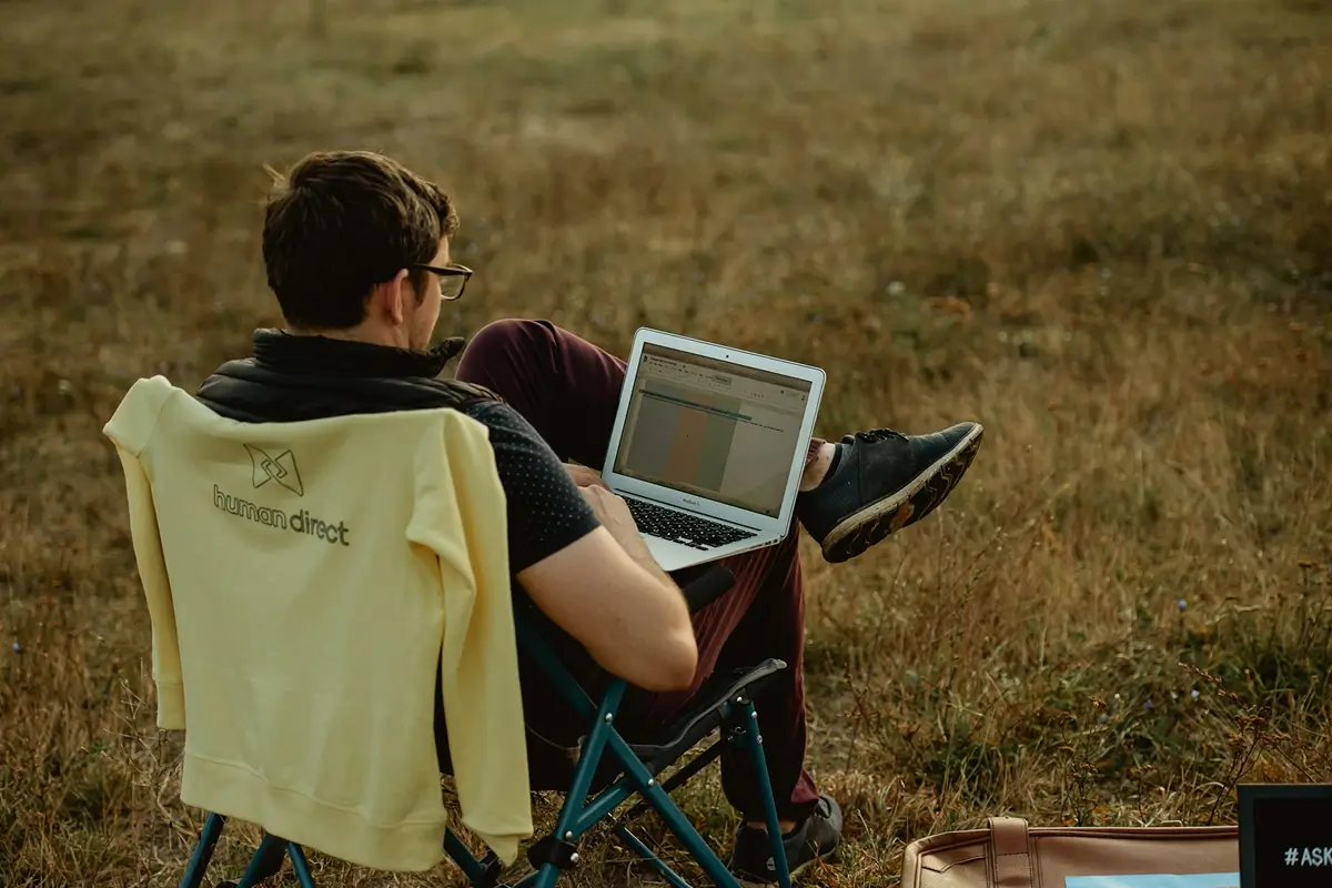 An economics professional working from a laptop while sitting in a chair outdoors, illustrating flexible work arrangements.