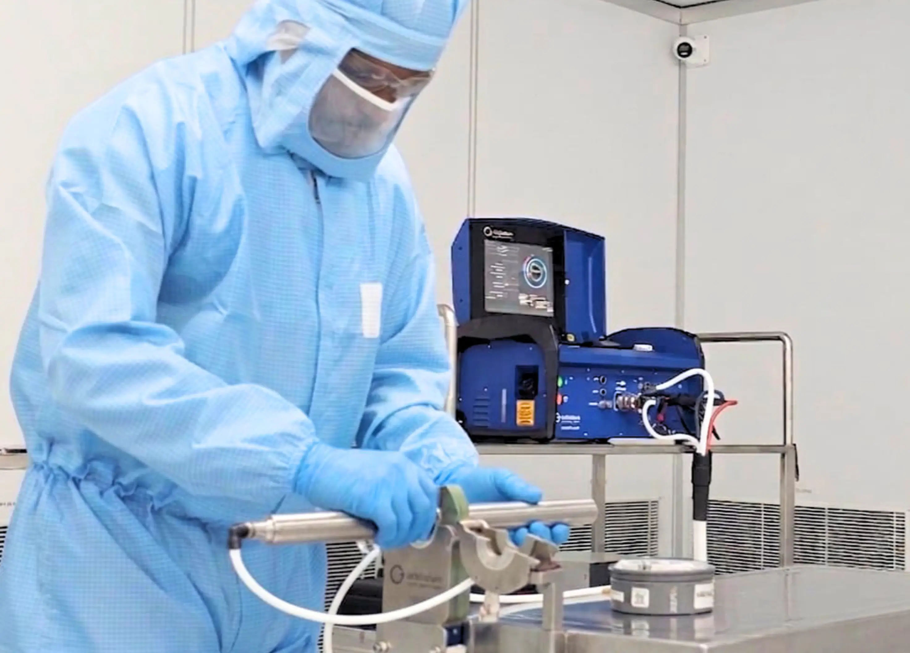 Person in blue protective suit and face shield handling scientific equipment in a lab setting.