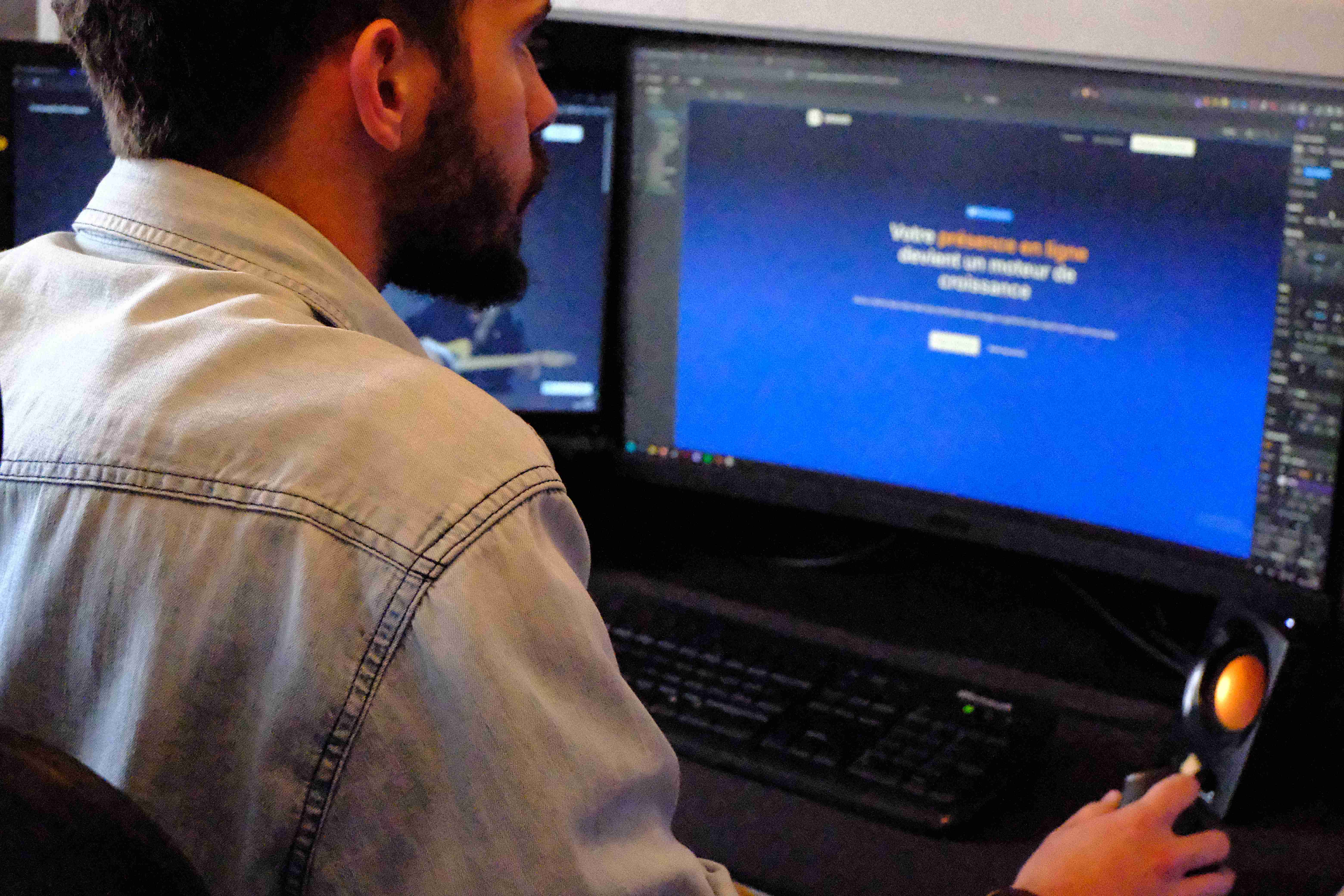 Jeune homme travaillant sur un ordinateur avec deux écrans, concentré sur la tâche.
