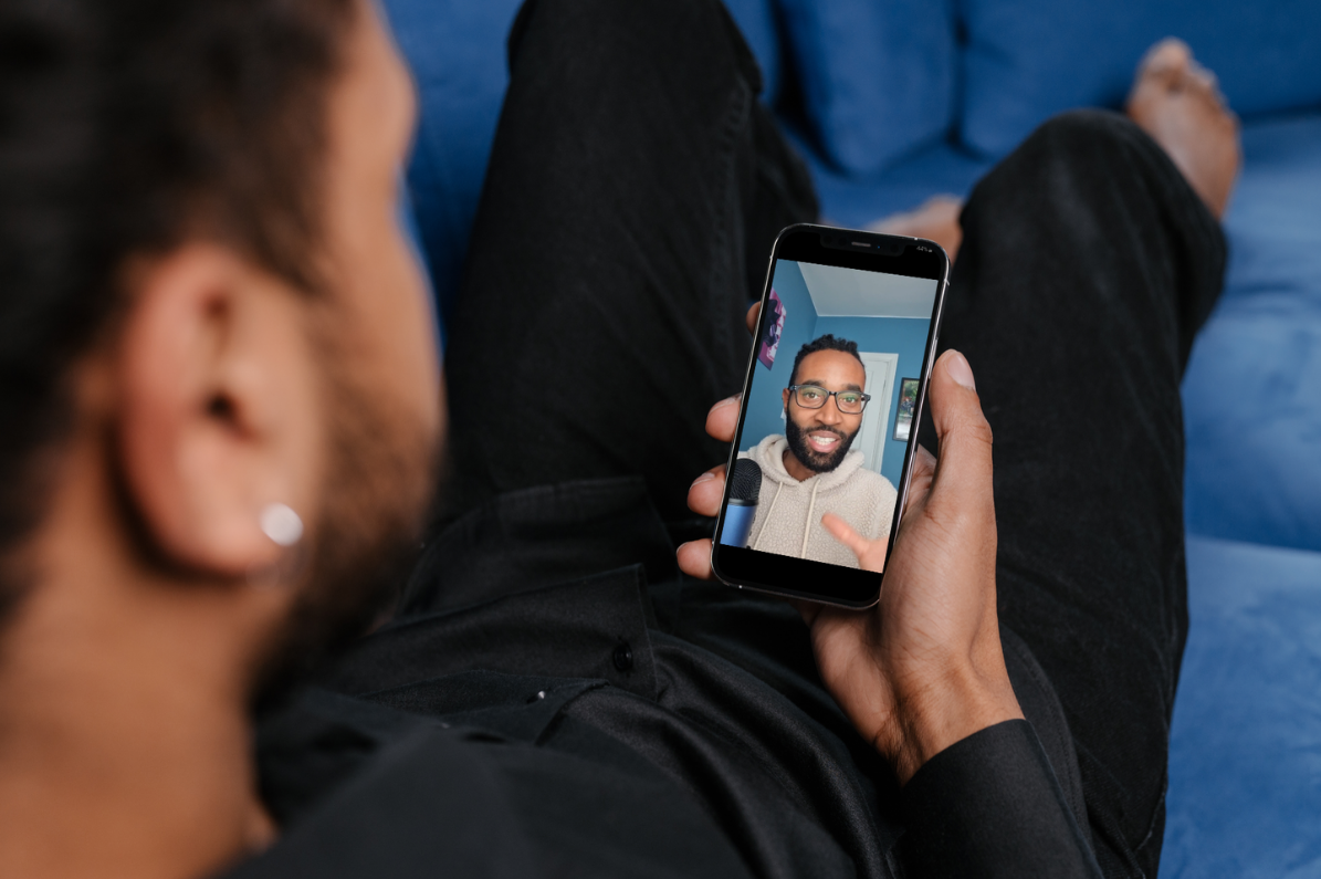 A man sat on a sofa holding a mobile talking to Dr Lewis Thomas on video call