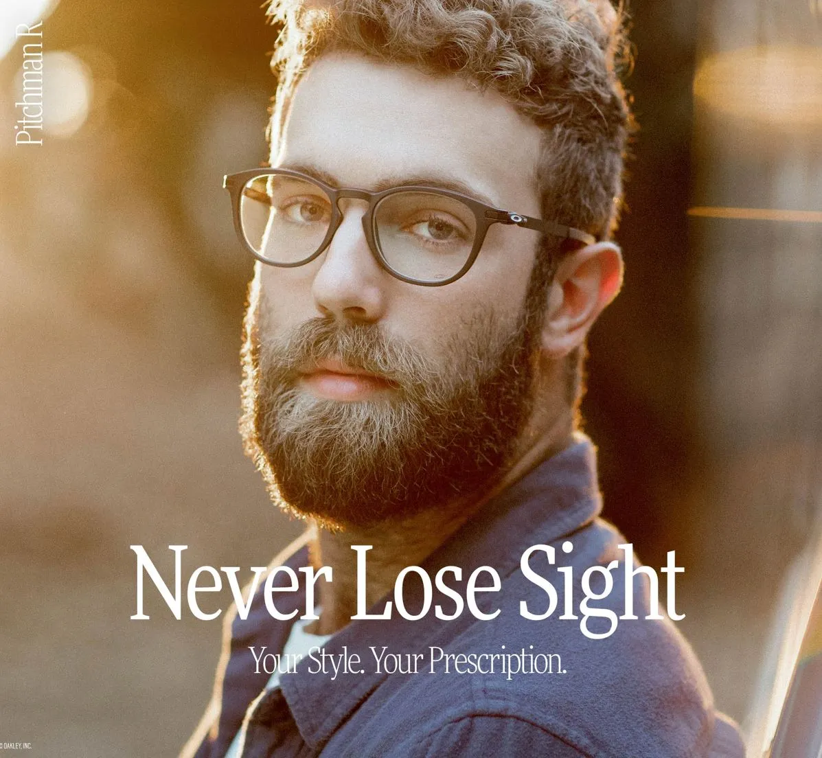 Bearded man with curly hair wearing clear prescription glasses in warm natural light.