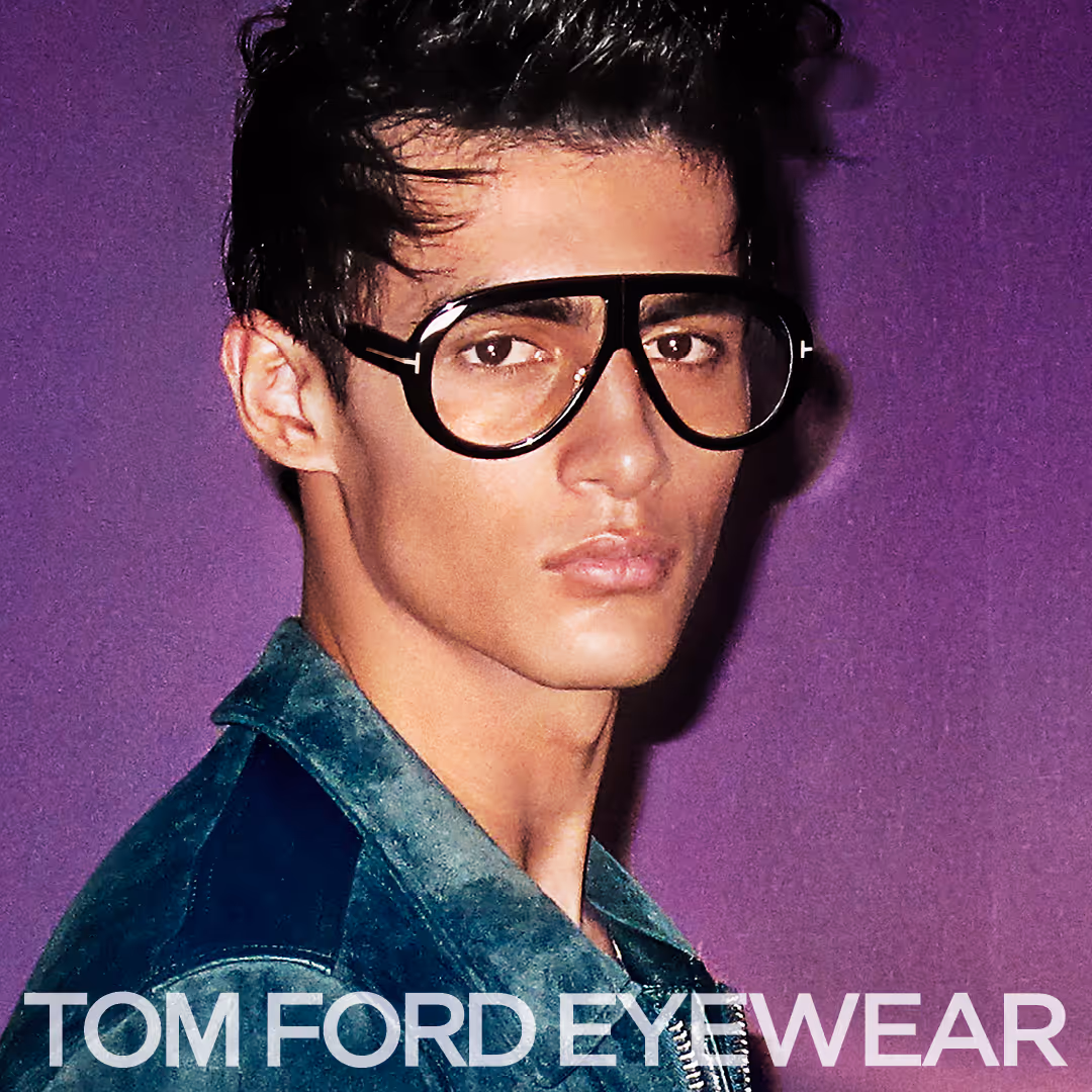 Young man wearing large black-framed Tom Ford eyeglasses against a purple background.