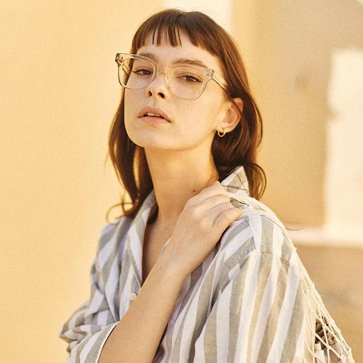 Young woman with short brown hair and clear glasses wearing a striped shirt against a beige background.