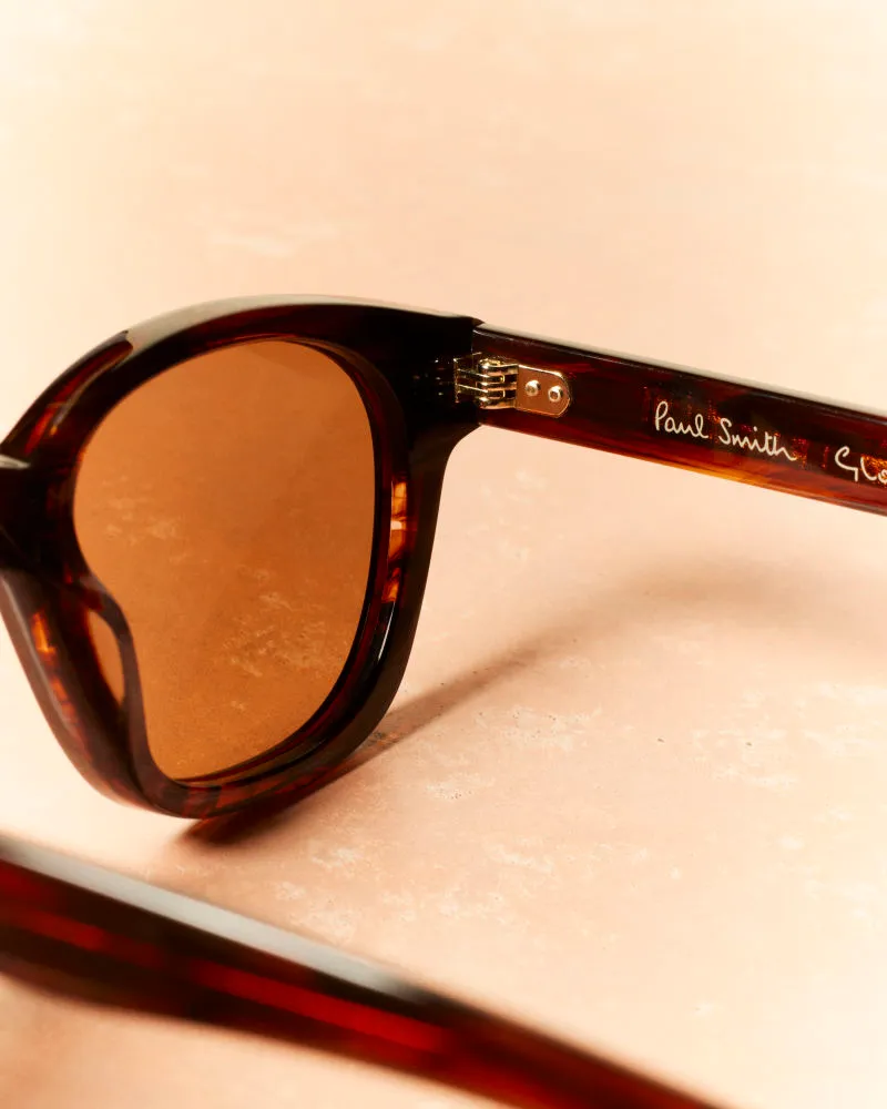 Close-up of brown tortoiseshell sunglasses with brown lenses on a beige surface.