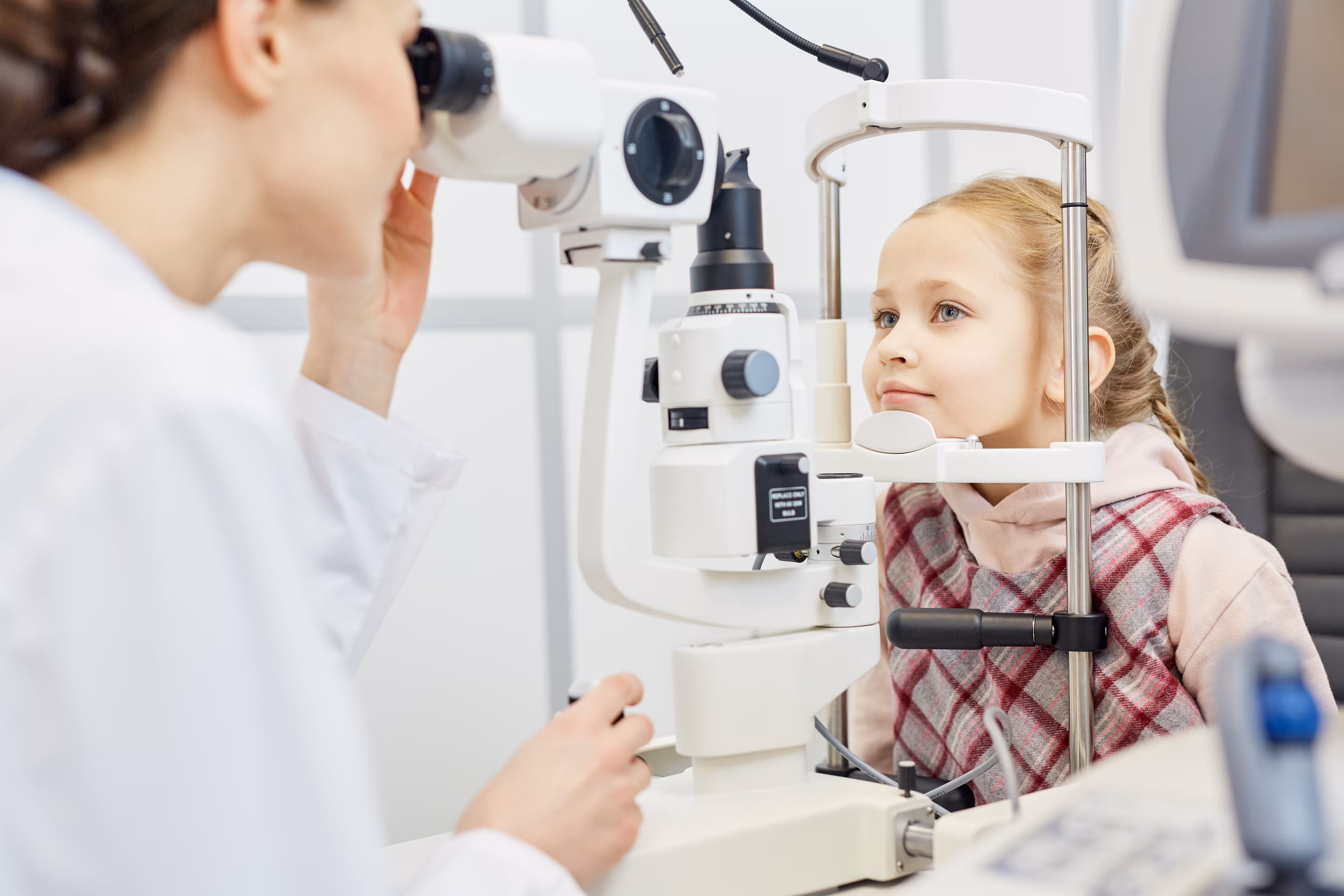 Young girl having an eye exam with slit lamp by an optometrist in a white coat.