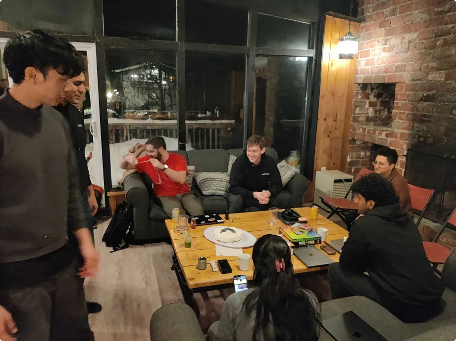 Group of friends socializing around a coffee table with drinks and snacks in a cozy living room.