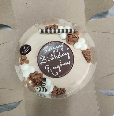 Round chocolate birthday cake with white and brown cream decorations and text Happy Birthday Raghav.