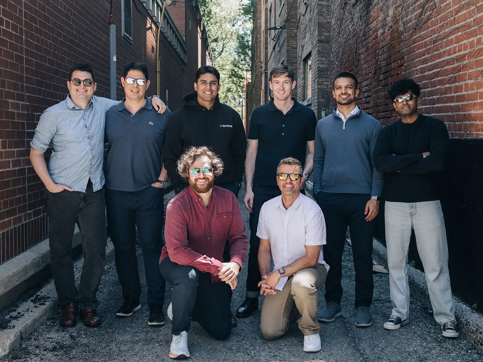 Eight men in an urban alley posing, with two kneeling in front and six standing behind.
