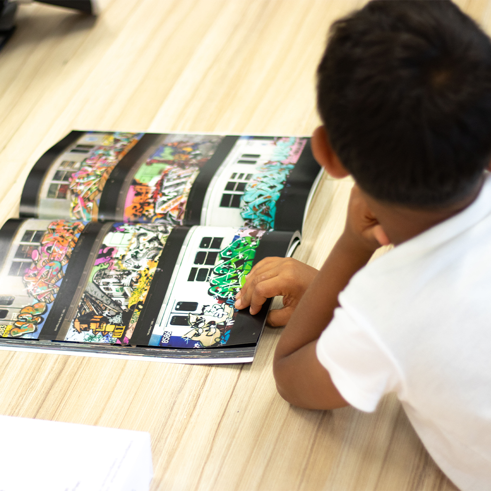 Un enfant allongé sur un plancher en bois, regardant un magazine présentant des graffitis colorés sur des bâtiments.