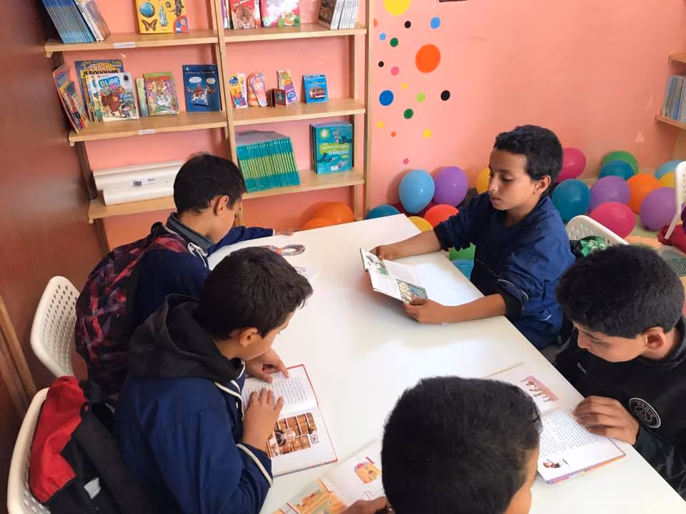 Child reading an illustrated book with Arabic text and a drawing of a yellow animal holding a white object near a colorful doorway.