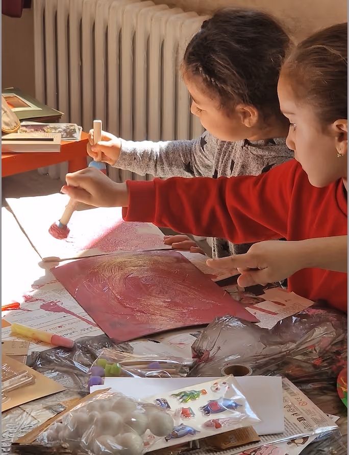 Child and woman sitting at a table in a library, smiling and looking at a small book together.