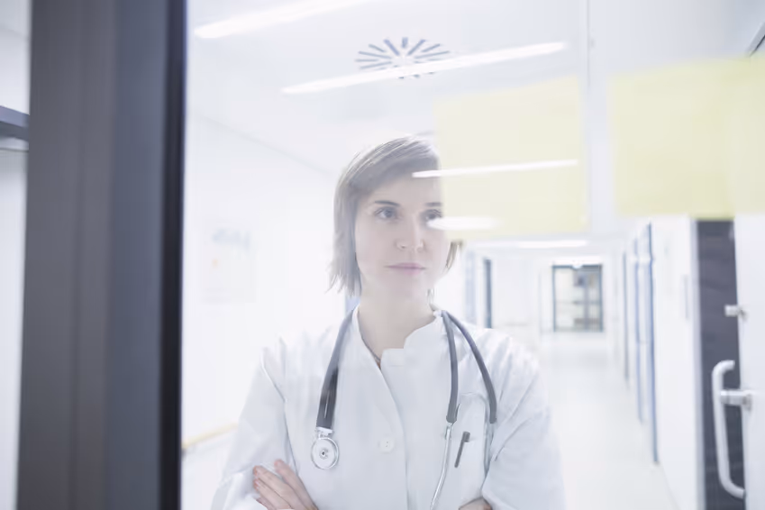 Une cadre de santé regarde de manière perplexe à travers une fenetre, symbolisant sa frustration face à la difficulté de son établissement de santé à attirer du personnel paramédical.