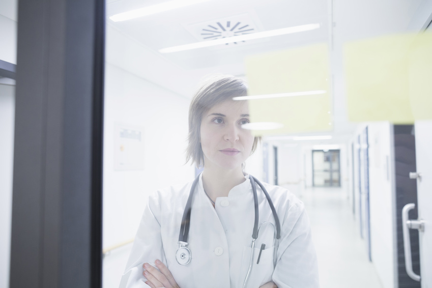 Une cadre de santé regarde de manière perplexe à travers une fenetre, symbolisant sa frustration face à la difficulté de son établissement de santé à attirer du personnel paramédical.