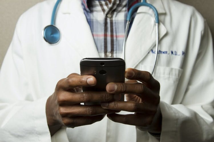 Gros plan sur les mains d'un cadre de santé, qui tiennent un smartphone, afin d'illustrer son utilisation d'outils numériques pour gérer ses besoins de remplacements.