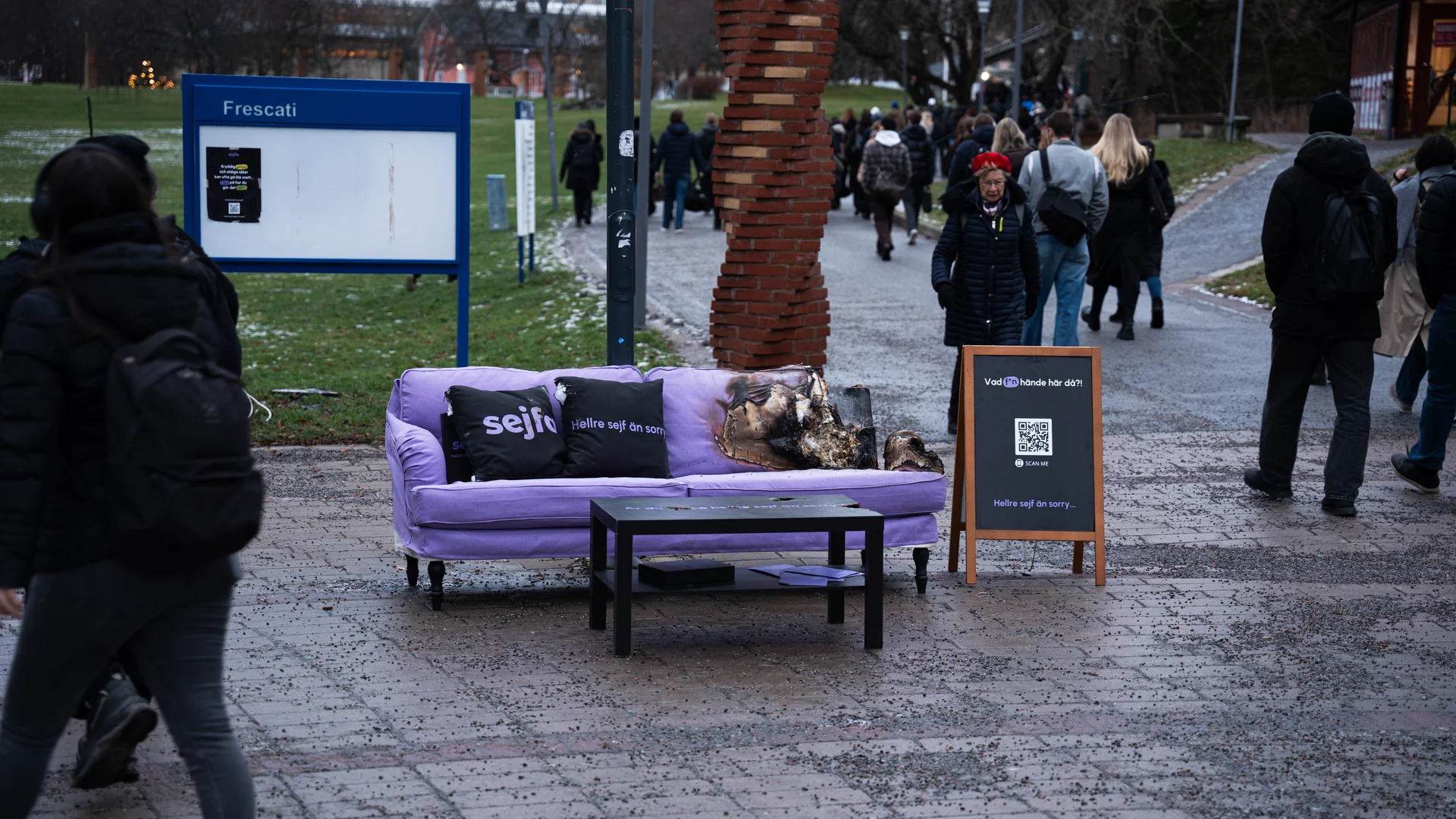 Kvinna med lockigt blont hår i grå tröja och blå byxor sitter i soffa med leopardmönstrad filt och gitarr bredvid.