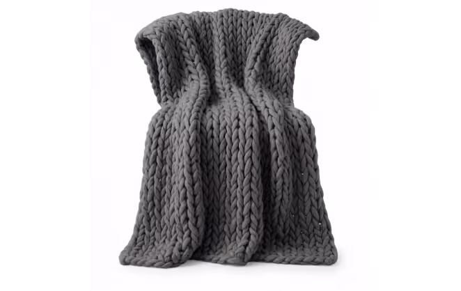 Thick chunky knit gray blanket draped in folds against a white background.