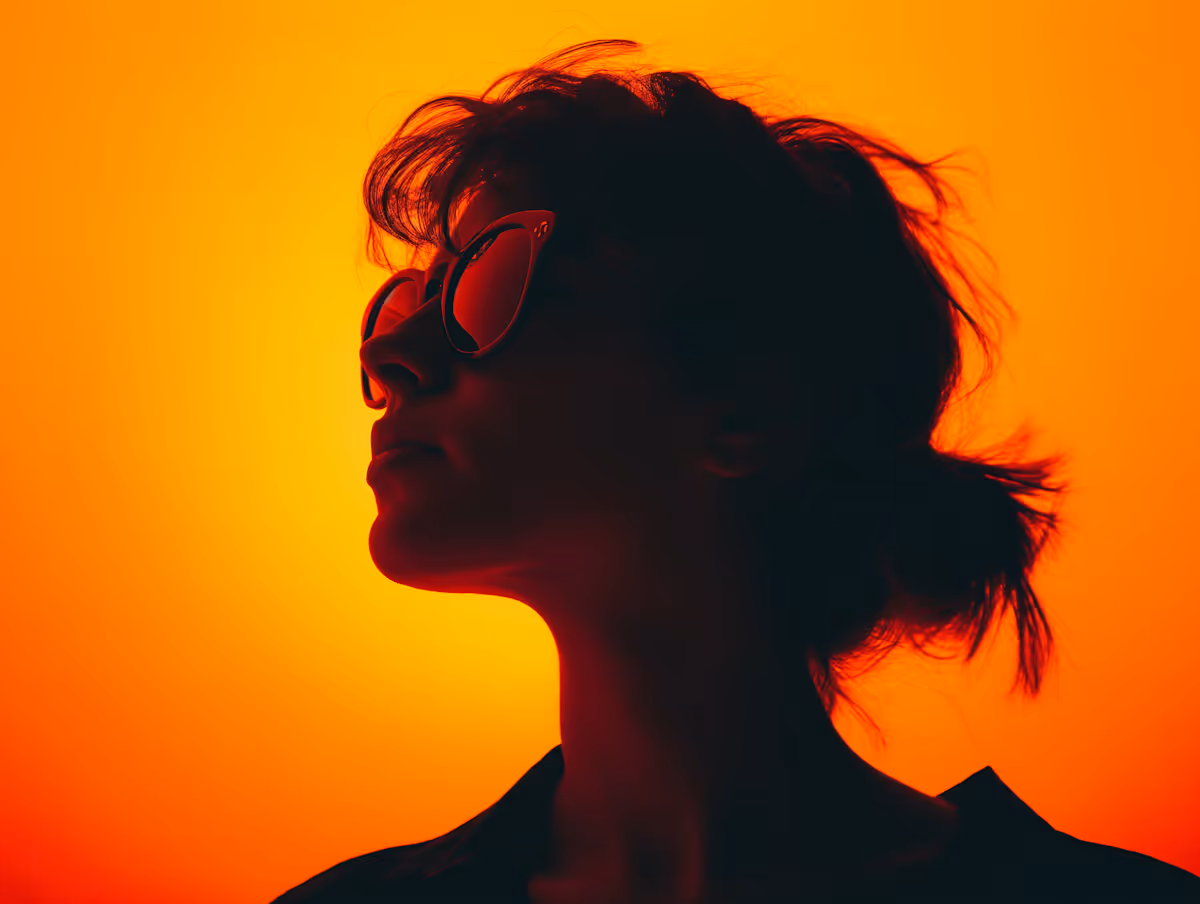 Silhouette of a woman wearing sunglasses against a vibrant orange sunset background.