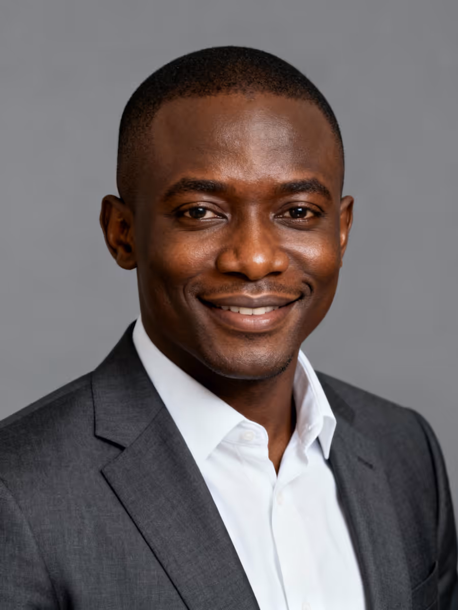 Smiling man wearing a dark gray suit jacket and white shirt against a gray background.