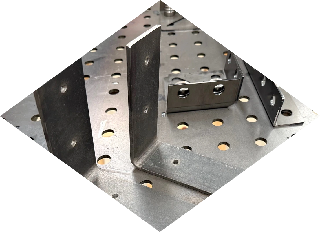 A diamond shaped transparent image of some metal brackets laying on a metal workbench.