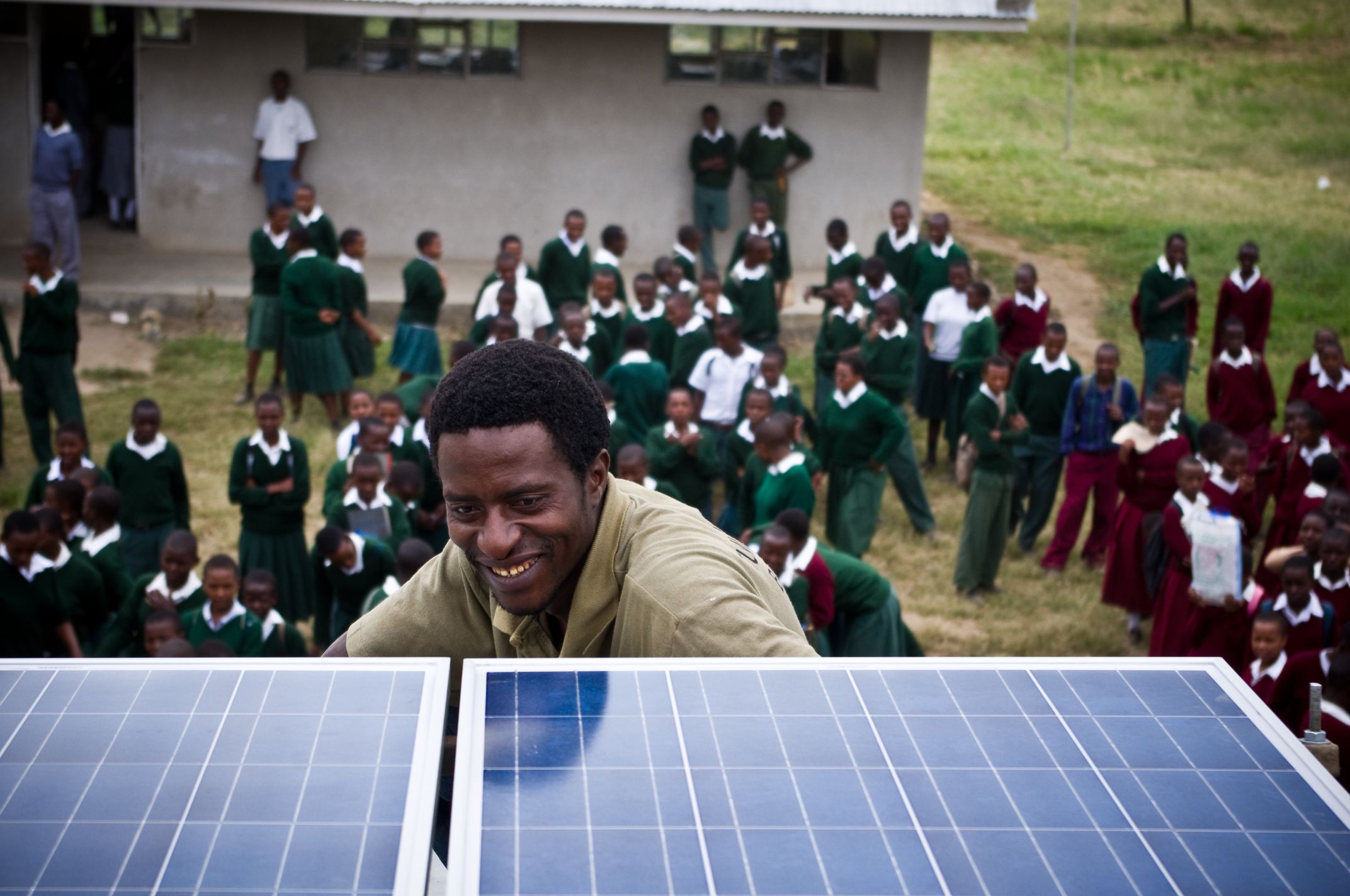 Smiling man looking at solar panels with school children in background