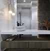 bathroom remodel with a large mirror, white marble wall, and a wooden vanity with a metallic faucet.